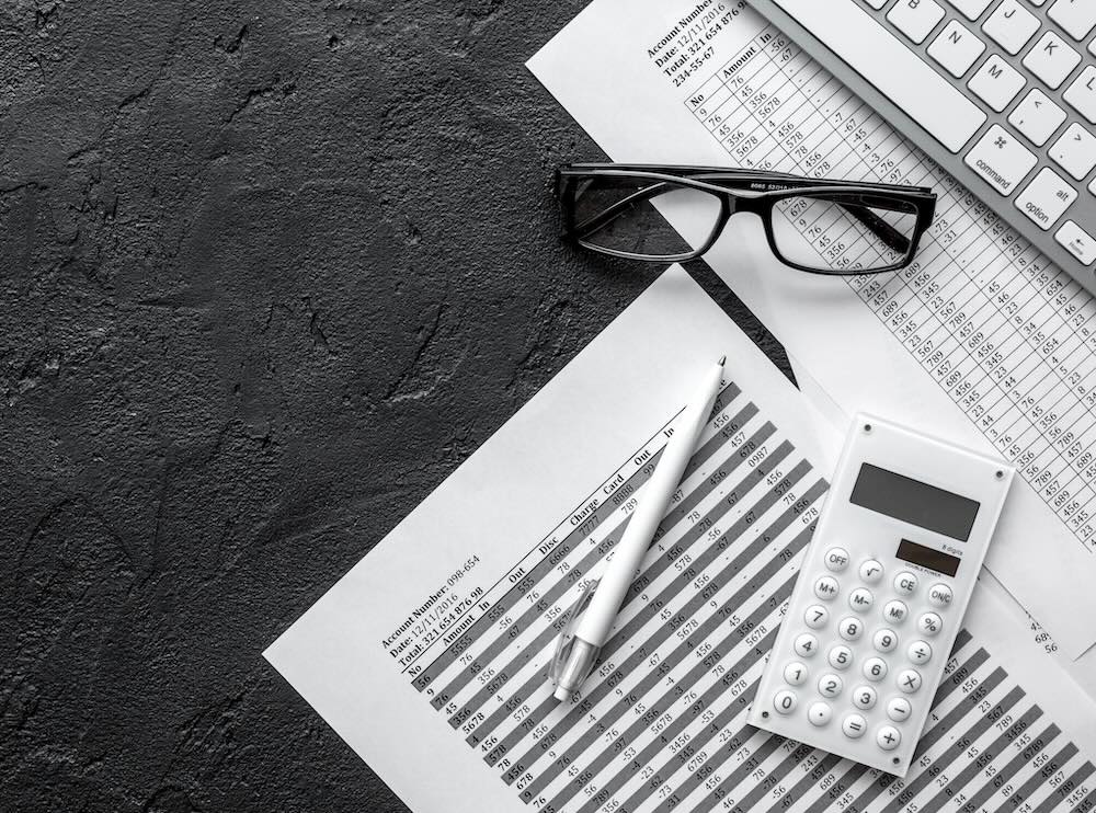 Photo of an office desk from above with documents, glasses and a calculator laying on top of it